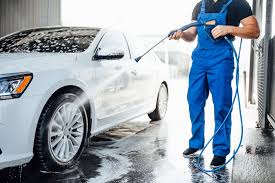 A man in blue overalls washing a white car.